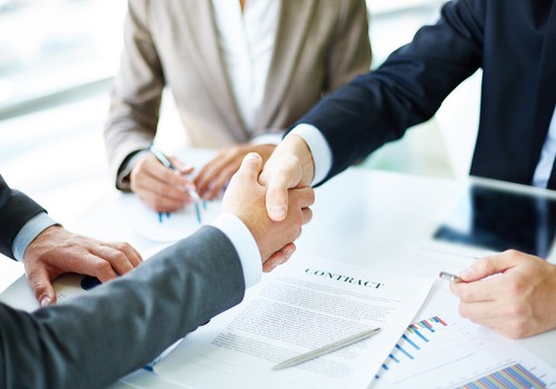 Image of business partners handshaking over business objects on workplace